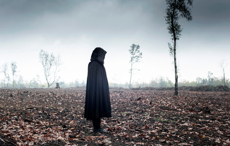 Woman in black cape in moody landscape.の写真素材