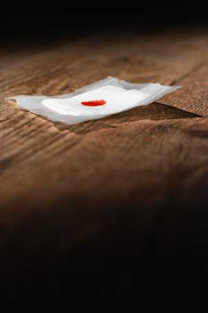Used bandage with blood spot fallen on wooden floor.