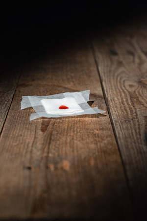 Used bandage with blood fallen on wooden floor in strip of light.の写真素材