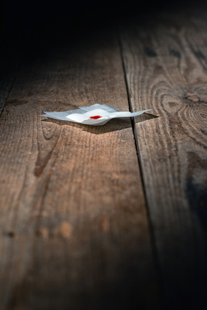 Used bandage with blood fallen on wooden floor in strip of light.の写真素材