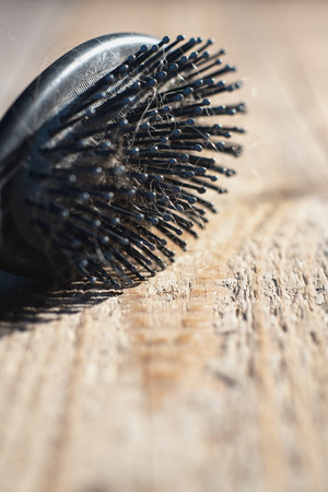 Black hairbrush with blonde hair on wooden floor.の写真素材