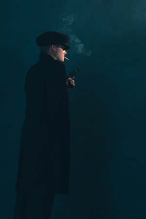 Retro mobster with cigarette holds gun. Side view.