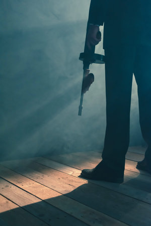 Retro gangster stands with machine gun in smoky room. Rear view.