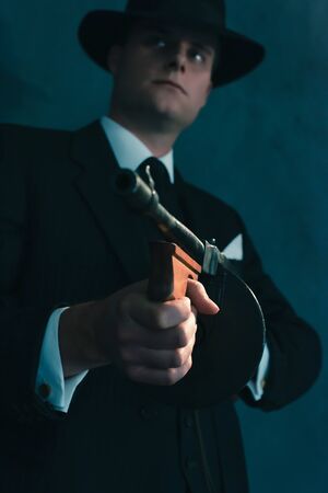 Retro gangster in hat shoots with machine gun.の写真素材