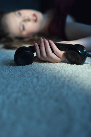 Murdered woman in red dress holding vintage telephone in her hand lying on floor.の写真素材