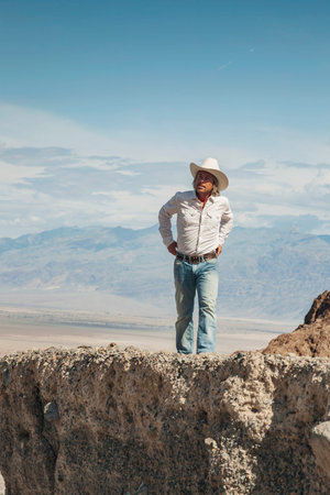 Man in white cowboy hat on a rock in a desert landscape.