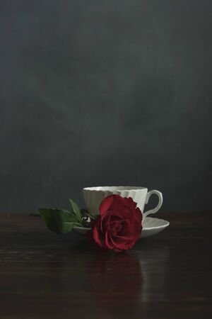 White china cup and saucer with red rose on wooden table.の写真素材