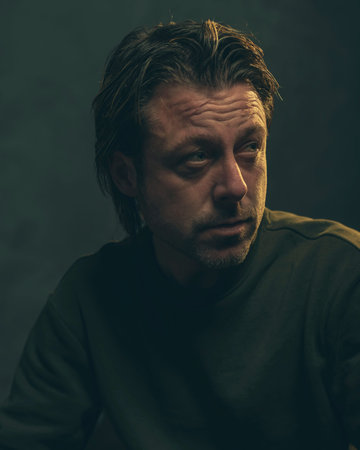 Middle aged man with stubble beard in green sweater.