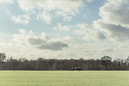 Tractor in sunny countryside under blue cloudy sky.