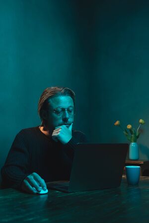 Man with eyeglasses working at home behind laptop in the evening.の写真素材