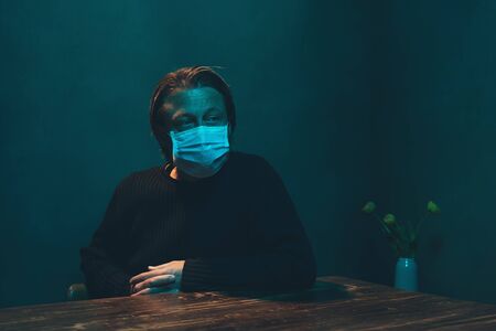 Man with protection mask sits at table in room in the night.の写真素材