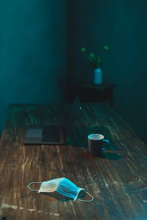 Hygienic mask on wooden table with laptop and cup of coffee.の写真素材