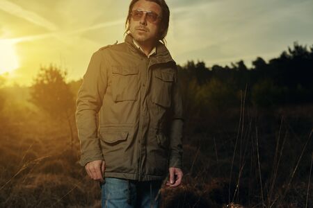 Man in green jacket and sunglasses in nature at sunrise during spring.の写真素材