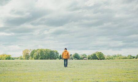 Man in yellow jacket and jeans walks in meadow in countryside.の写真素材
