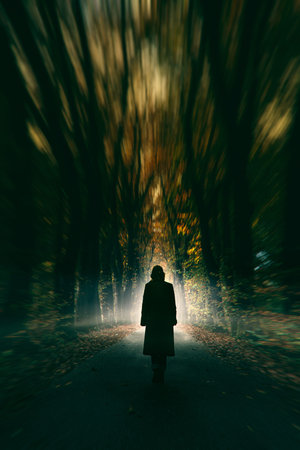 Woman in black coat walks on misty forest road in autumn.