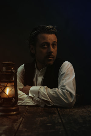 Vintage victorian style man behind wooden table with historical oil lantern.の写真素材