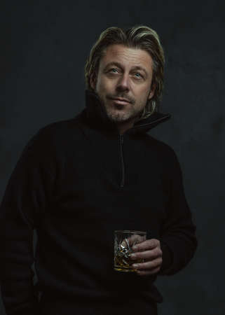 Blond man in black woolen sweater holding glass of whiskey.の写真素材