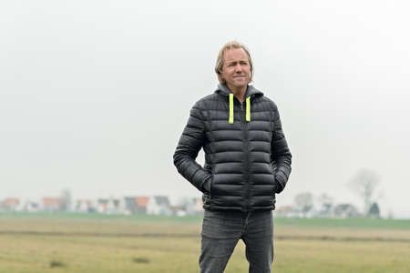 Blonde middle aged man in black jacket in misty rural landscape.の写真素材