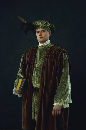Renaissance man holding a book stands in front of a dark wall.