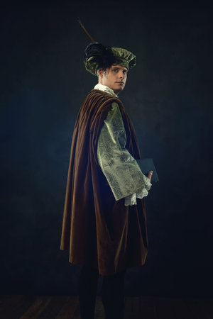 Renaissance man holding a book stands in front of a dark wall.