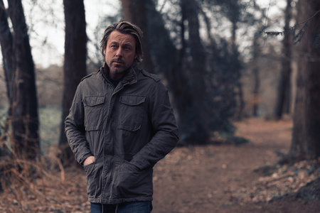 Blonde man in a green coat walks on a forest path.