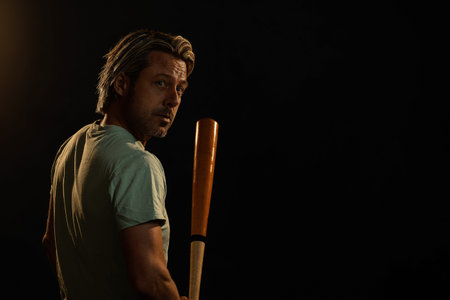 Blonde man in a light green t-shirt stands with a baseball bat.