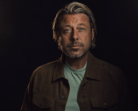 Middle-aged man with a stubble and blond hair wears a brown corduroy jacket with a light green...
