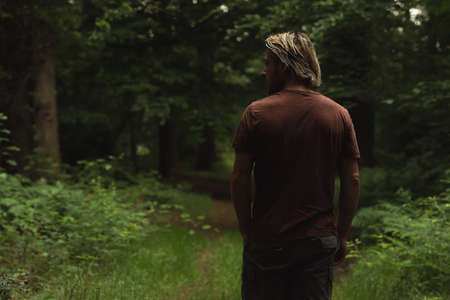 Blonde man in brown t-shirt on a forest path in summer. Rearview.の写真素材