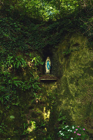 Virgin Mary statue in a rock wall in a lush green forest.の写真素材