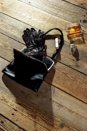 Ladies beauty accessories spilled out of a black leather handbag fallen on a wooden floor.