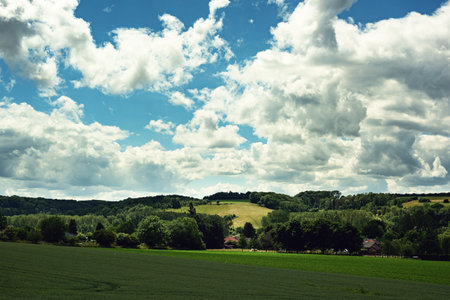 Houses in a rolling lush landscape in the countryside under a blue cloudy sky on a sunny summers...