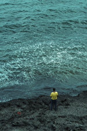 Man in a yellow t-shirt stands on a pebble beach near the sea water. top view.の写真素材