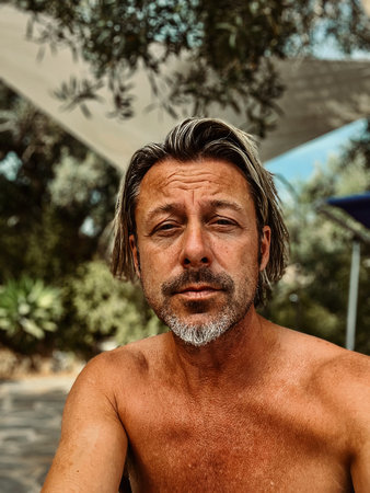 Ttanned man with stubble beard and blond hair enjoying summer garden with olive trees.の写真素材