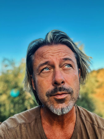 Middle aged man with blond half long hair and grayish beard outdoor in nature on a sunny day....