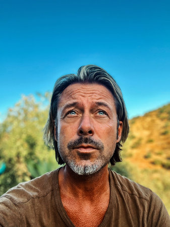 Middle aged man with blond half long hair and grayish beard outdoor in nature on a sunny day....