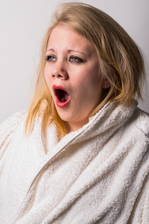 disheveled morning tired young woman yawning  wearing a white bathrobeの写真素材