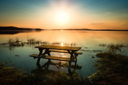 beautiful picture of a table with bench by a lake with the sun and sunbeams in the skyの写真素材