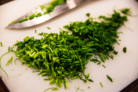 chopped chives on a white cutting board with a knife in the backgroundの写真素材