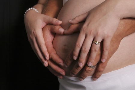 Closeup of parents hands shaped as heart against pregnant tummy, black backgroundの写真素材