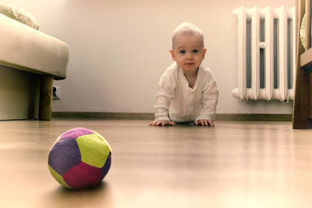 Baby on the floor is going to crawl towards the ball.