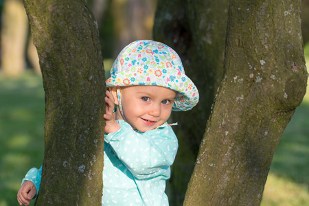 Cute, one-year-old smiling baby girl outdoors. She poses among the trees.の写真素材