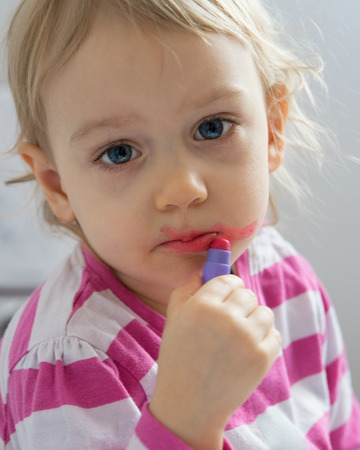 Two-year old girl paints lips with lipstick. Child portrait 4:5.の写真素材
