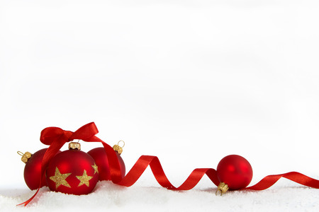 Four Christmas balls with red ribbon on artificial snow flakes.の写真素材
