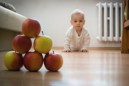 Baby on the floor is going to crawl towards stack of apples.
