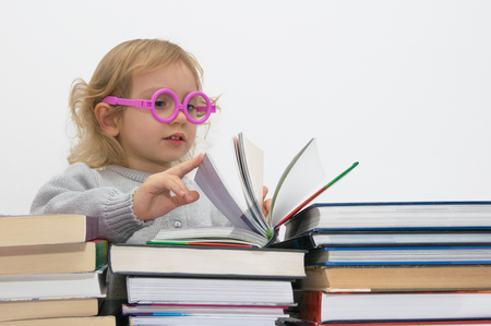 Three year old girl in pink glasses absorbed in reading  book.の写真素材
