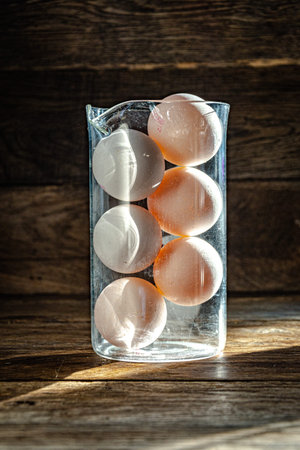 Eggs in a transparent glass container on a wooden background. Six white chicken eggs in a glass...