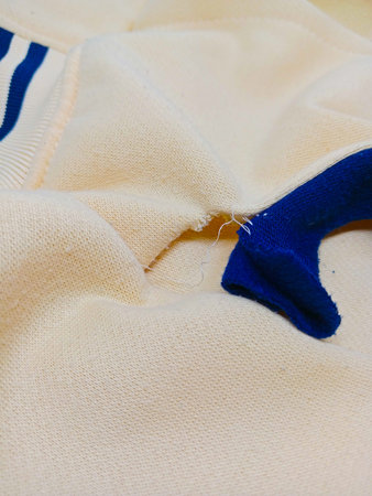 Closeup detail of ripped beige sweater pocket. Macro shot