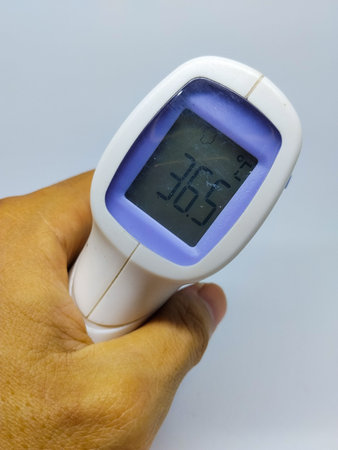 hand holding a digital thermometer showing a normal body temperature of 36Â°Celcius