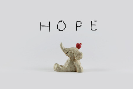 statue toy of smiling elephant with apple looking up over hope wordings background. Idea of happy, warm message concept for pattern background, card, decoration wallpaper, design templateの写真素材