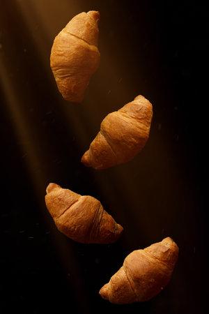Several croissants on a black background illuminated by rays.